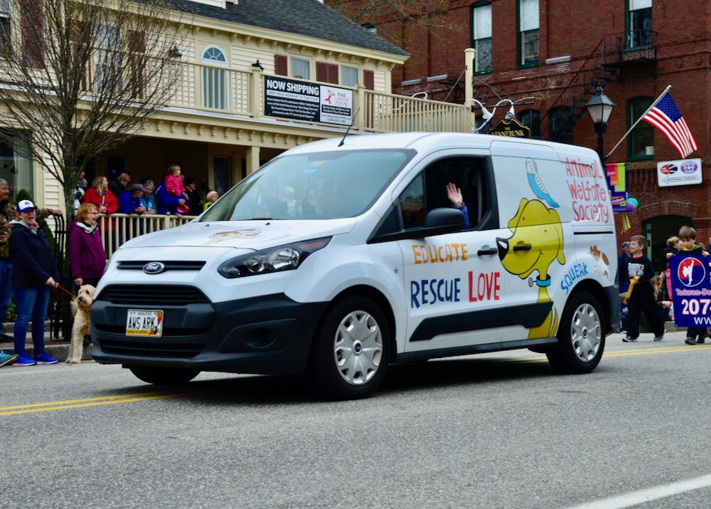 white van with a large cartoon dog and bird on side drives in a parade