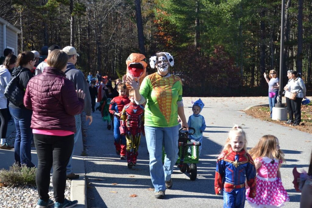 children and adult walk in a halloween parade on a paved sidewalk