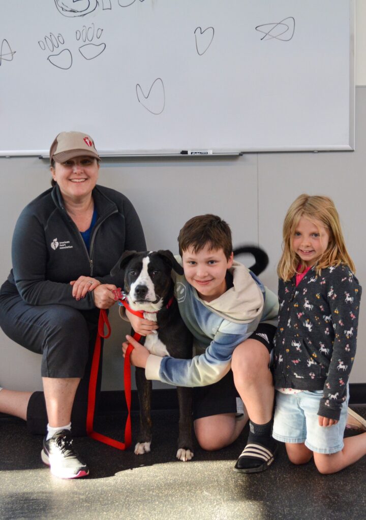 Mother and two children pose with black and white dog with a red leash