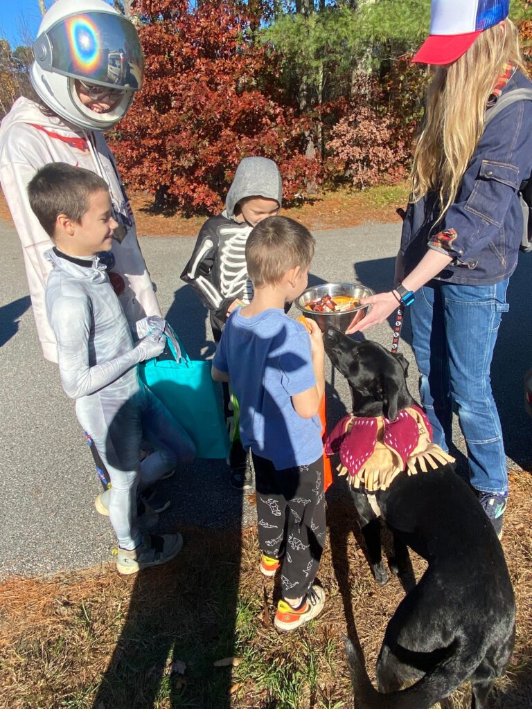 children in costume trick or treat outside with a black dog