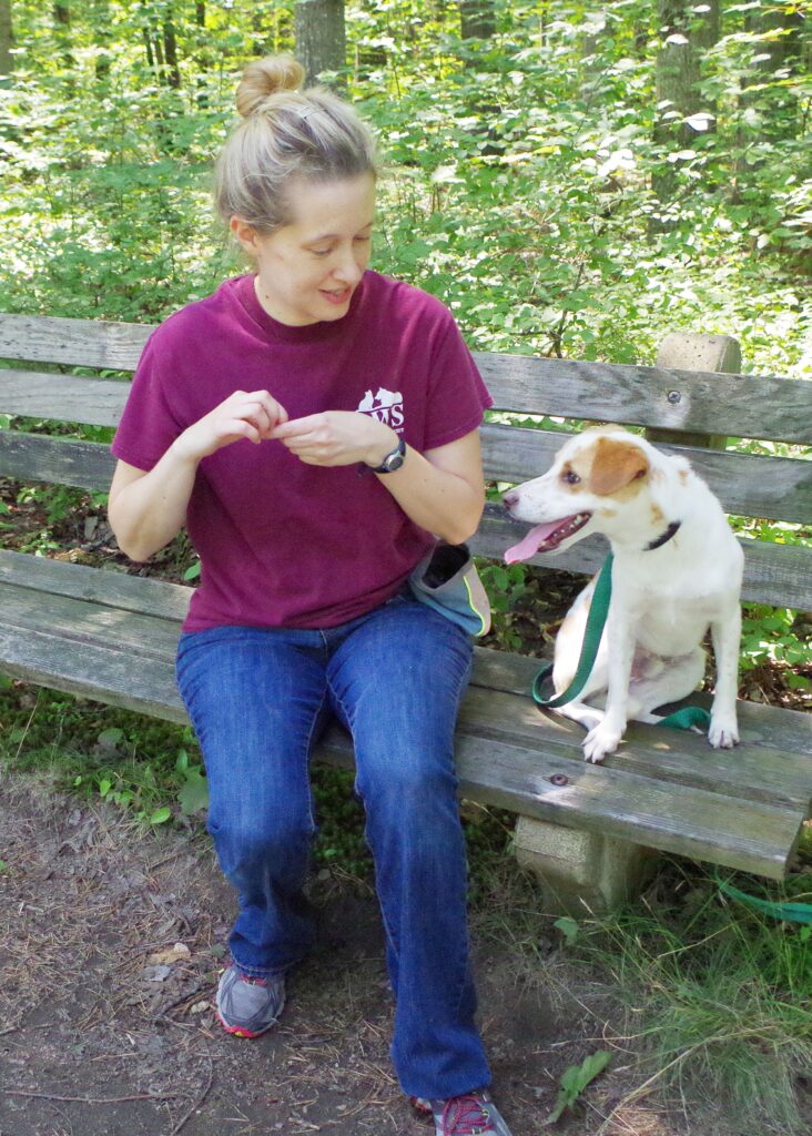 woman and dog sit on bench. Woman is giving dog treats
