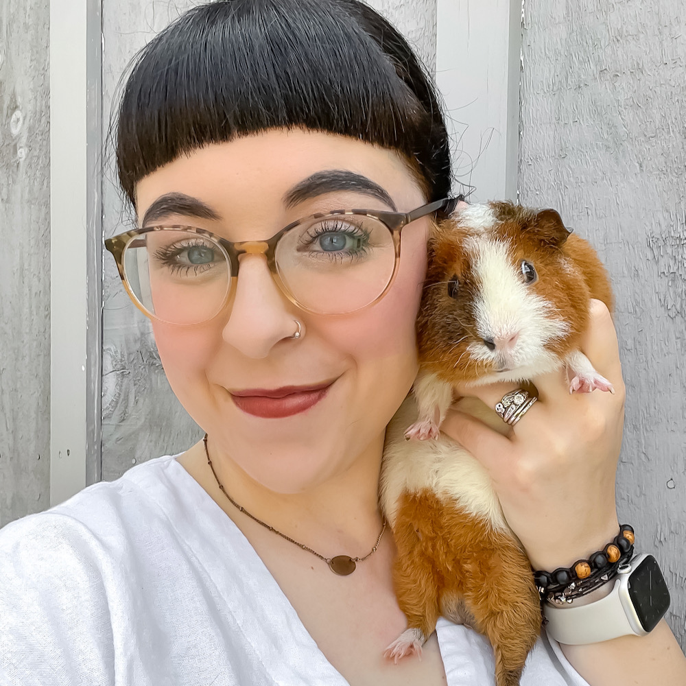 A woman smiles at the camera while holding a red and white guinea pig up to her face