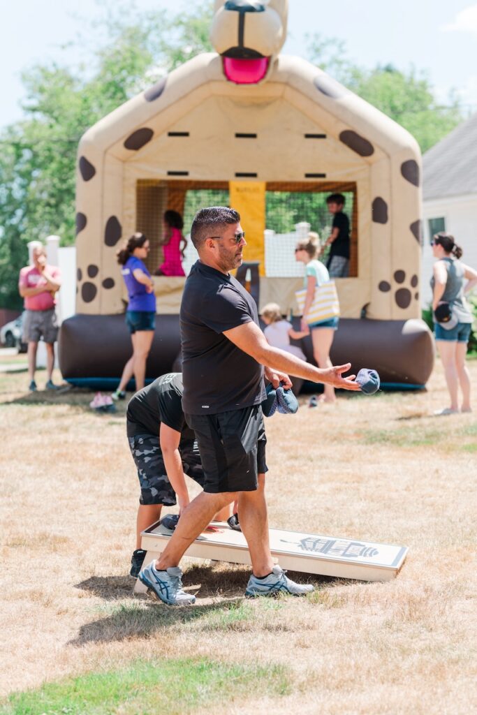 man plays cornhole with bounce house in the background at Woofstock Festival