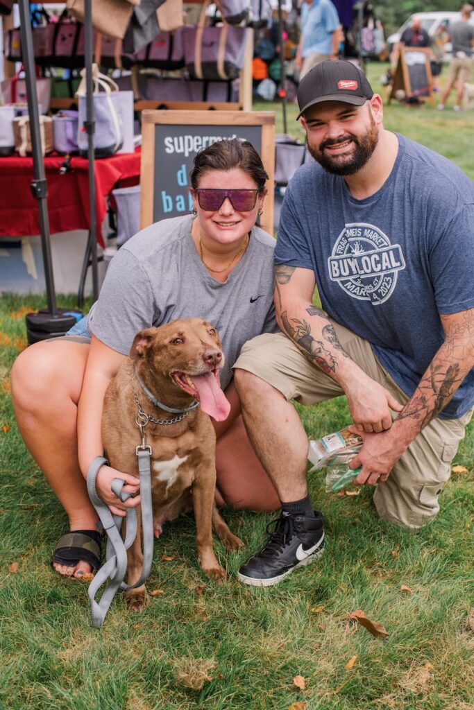 couple and dog pose in front of shopping tents at Woofstock Festival