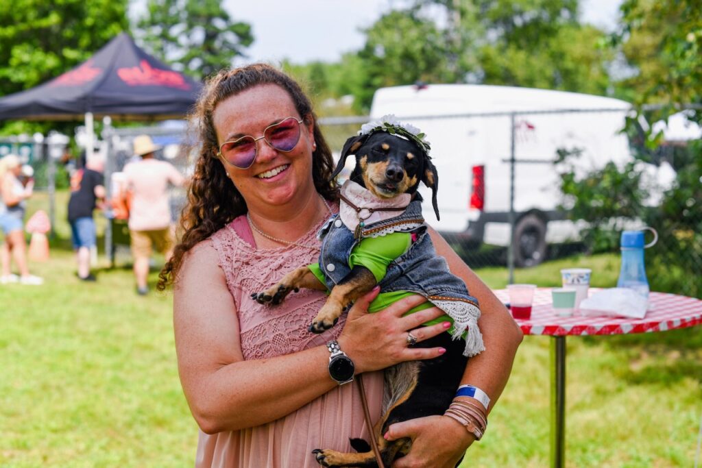 woman holds dog dressed in 1960s attire at Woofstock Festival