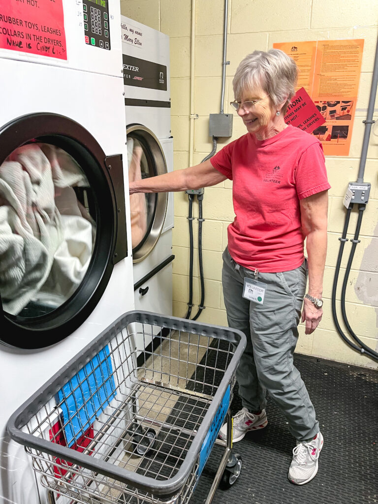 woman in red shirt stands by washing machine and dryer