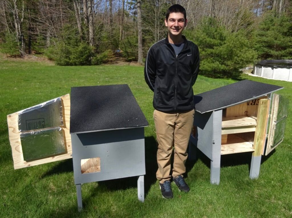 boy scout stands next to newly constructed cat houses