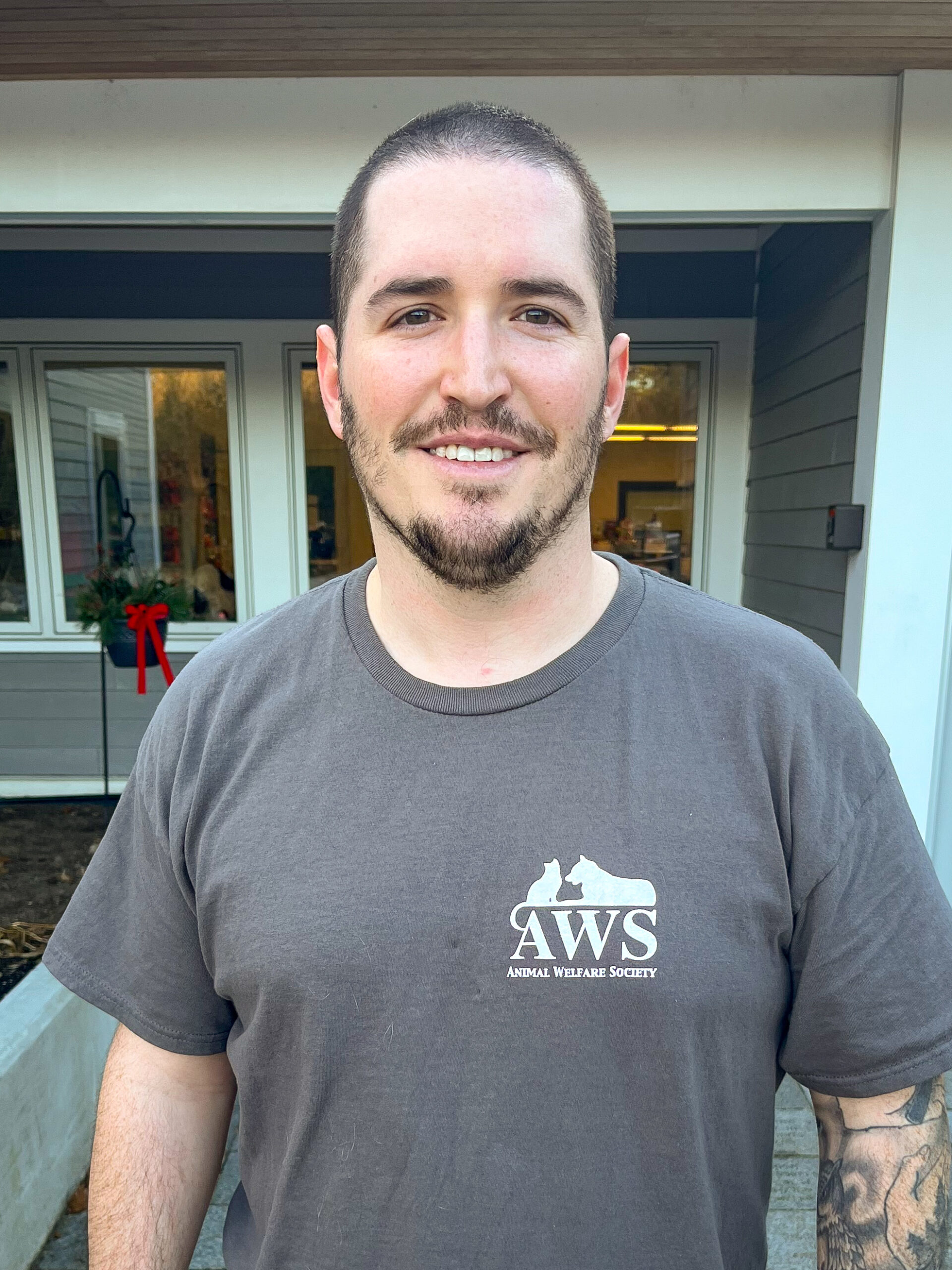 Man wearing an AWS shirt smiles at camera in front of building.