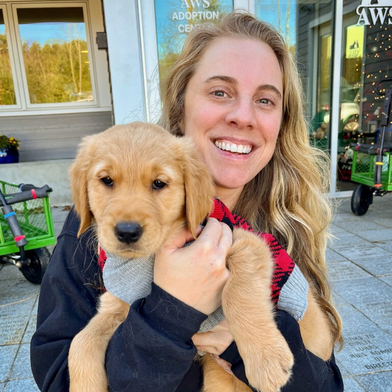 A woman holds a young puppy in front of the AWS Adoption Center building.