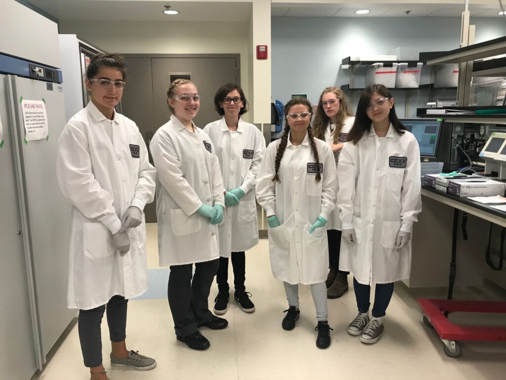 six high school students in white lab coats pose in a laboratory