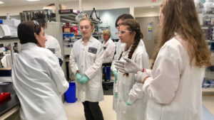 High-school students in IDEXX lab coats learn from a lab specialist.