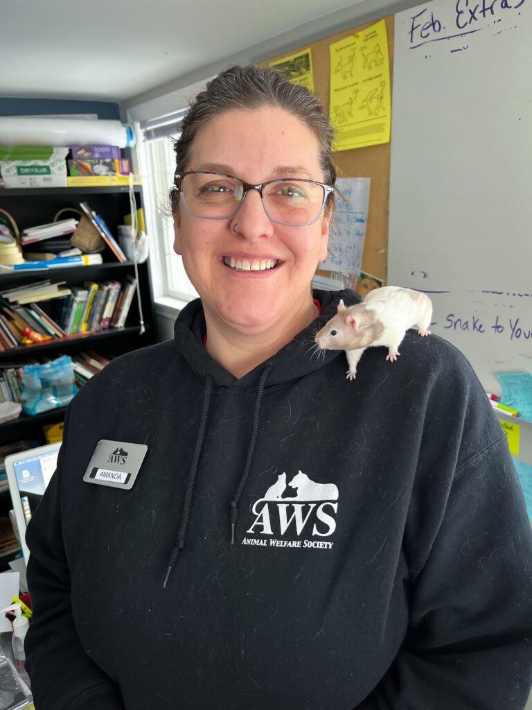 Woman in an AWS sweatshirt smiles at the camera while a hamster sits on her shoulder. 