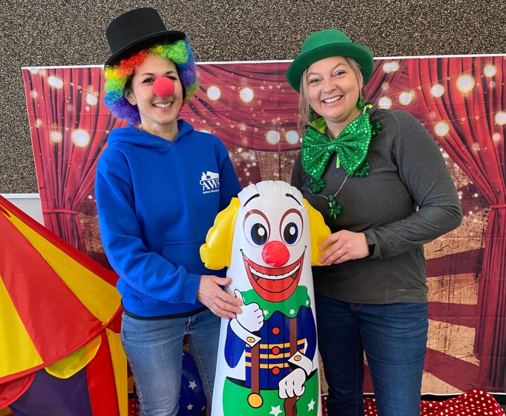 Two people wearing funny outfits posing with a clown doll during Circus Dog Class.