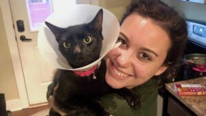 A woman holds a cat wearing a medical cone while smiling at the camera.