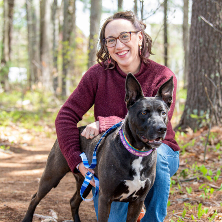 Suz is posed on one knee with a black dog with pointy ears standing just in front of her