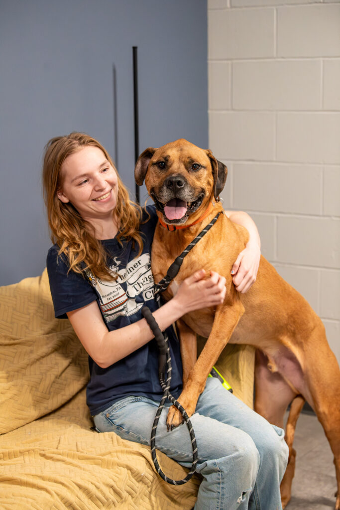 Apollo the adoptable dog at Animal Welfare Society cuddles up with an Animal Care Tech on a couch. Pet of the Week 2026.